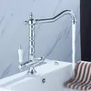 A chrome kitchen faucet with white ceramic handles is shown in a bathroom or kitchen sink, with water running. Náhled obrázku produktu
