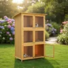 A wooden multi-level rabbit hutch with several compartments, some containing rabbits, set in a garden with flowers and grass. Podgląd zdjęcia produktu
