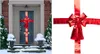 A large red bow is attached to a dark blue front door, decorated for winter with snow on the steps and urns. The image is split, with the door decoration on the left and a close-up of the bow on the right. Náhled obrázku produktu