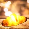 A croissant-shaped LED night light sits on a wooden surface with a blurred background of warm lights. Podgląd zdjęcia produktu