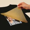 A hand is holding a transfer sheet over a black t-shirt with a printed image of a man's face. Anteprima dell’immagine prodotto