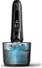 A black electric shaver is shown in its cleaning station, which contains blue liquid. Náhled obrázku produktu