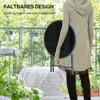 A person is holding a round, foldable table on a balcony with plants and furniture in the background. Produktbild-Vorschau
