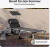 A grey reclining sun lounger with a canopy and side pocket is set up on a wooden deck next to a small grey table with a drink on it. The background is a textured wall. Anteprima dell’immagine prodotto