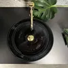 A black glass vessel sink with a gold faucet and a monstera leaf in the background. Produktbild-Vorschau