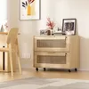A wooden filing cabinet with two drawers on wheels, placed in a room with a chair and wall art. Náhľad obrázku produktu