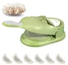 A green dumpling maker with a plate of dumplings in the background and several finished dumplings in the foreground. Produktbild-Vorschau