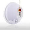 A white LED outdoor wall light with a motion sensor, displayed against a white background with a reflection. A tag with the German flag and the word 'DEUTSCHE MARKE' is hanging from the light. Produktbild-Vorschau