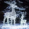 Two illuminated reindeer figures stand in the snow in front of a snow-covered evergreen tree at night. Anteprima dell’immagine prodotto