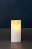 A white LED candle with a flickering yellow flame sits on a dark surface against a dark blue background. Produktbild-Vorschau