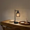 A black metal desk lamp with a spiral cage shade sits on a wooden desk next to a stack of books and a tray with a small dish and a ceramic holder with two sticks. Podgląd zdjęcia produktu