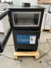 A modern black wood-burning stove with an open door and a visible oven rack, placed on a wooden pallet. Produktbild-Vorschau