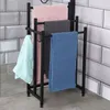 A black metal towel rack with four towels hanging on it, set against a tiled wall. Náhľad obrázku produktu