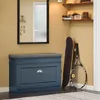 A blue shoe cabinet with a gray seat cushion is shown in an entryway, next to a mirror and shelves. A skateboard and tennis racket are leaning against the wall. Náhľad obrázku produktu