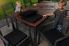 Two children are interacting around a table and chairs set with cushions, outdoors. Produktbild-Vorschau