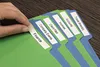 A hand is shown applying a label to a file folder, with several other labeled file folders visible. Náhled obrázku produktu