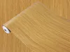 A roll of wood-grain patterned contact paper, partially unrolled, lying on a surface with the same wood grain pattern. Produktbild-Vorschau
