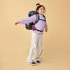 A young girl wearing a backpack and striped pants, with her arms outstretched. Náhled obrázku produktu