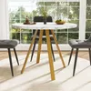 A round dining table with a marble-like top and gold legs, set in a bright room with large windows overlooking a garden. Two gray upholstered chairs are placed around the table. Produktbild-Vorschau