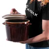 A person is holding a brown ceramic pot with a lid. Voir les images du produit