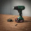 A cordless drill with battery and charger on a wooden table. Produktbild-Vorschau