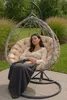 A woman is relaxing in a hanging egg chair outdoors, covered with a blanket. Produktbild-Vorschau