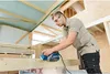 A man is using a power planer on a piece of wood in a construction setting. Anteprima dell’immagine prodotto