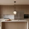 A modern kitchen with wooden cabinets, marble countertops, and a stainless steel refrigerator. A pendant light hangs over a kitchen island with a loaf of bread and a mug. Náhled obrázku produktu