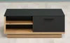A modern coffee table with a black top and drawer front, and a wooden frame and shelves, is shown in a room with light wood floors and a pale blue wall. Voir les images du produit