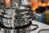 A stack of shiny metal pots and pans with glass lids, some with the Tefal logo visible. Náhled obrázku produktu