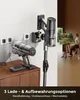 Two cordless vacuum cleaners are shown, one on a charging stand and another mounted on a wall charger. A person is painting in the background. Produktbild-Vorschau