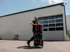 A man is pushing a stack of toolboxes on a trolley in front of a large industrial building. Produktbild-Vorschau