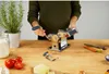 A person is using a pasta maker on a wooden table, surrounded by ingredients like tomatoes, carrots, and flour. Anteprima dell’immagine prodotto