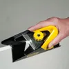 A hand holding a yellow and black drywall edge planer. Voir les images du produit