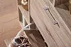A close-up view of a wooden shoe cabinet with a silver handle and a pair of shoes. Produktbild-Vorschau