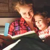 A mother and daughter are reading a book together in bed at night, illuminated by a small blue LED light. Produktbild-Vorschau