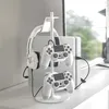 A white gaming accessory stand holding headphones and two controllers, with a white gaming console in the background. Produktbild-Vorschau