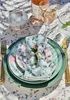 A table setting with plates, napkins, cutlery, and drinks, arranged on a floral tablecloth. Produktbild-Vorschau