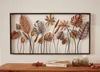 A metal wall art piece featuring various leaf designs is displayed on a wall above a wooden table with books and decorative apples. Produktbild-Vorschau