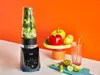 A blender with ingredients and a glass of juice are arranged on a table with an orange background. Anteprima dell’immagine prodotto