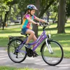 A young girl is riding a purple bicycle on a paved path in a park. Produktbild-Vorschau