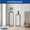 Two modern black metal plant stands of different heights are displayed in a living room setting, with plants on top. A gray sofa is visible on the right. Anteprima dell’immagine prodotto