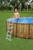 A man is standing in a wooden-look above-ground pool, holding onto the ladder. Produktbild-Vorschau