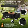 A black foldable wagon with a canopy is set up on a grassy area, with a picnic basket inside. Two people are blurred in the background. Produktbild-Vorschau
