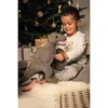 A young boy sits on a rug in front of a Christmas tree, holding a stuffed dinosaur. Produktbild-Vorschau
