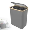A grey laundry basket with a wooden rim and a partially open lid, shown against a white background. A smaller, similar laundry basket filled with clothes is visible in the lower-left corner, next to a washing machine. Voir les images du produit