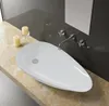 A white, tear-drop shaped vessel sink on a marble countertop with two candles and a faucet. Náhled obrázku produktu