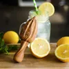 A wooden citrus juicer next to lemons and a glass of lemonade. Produktbild-Vorschau