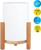 A white cylindrical lamp with a wooden base and legs, set against a white background. Icons indicating features are on the right side. Produktbild-Vorschau