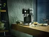 An espresso machine is set up on a wooden counter, with a shot of espresso and accompanying items nearby. Produktbild-Vorschau